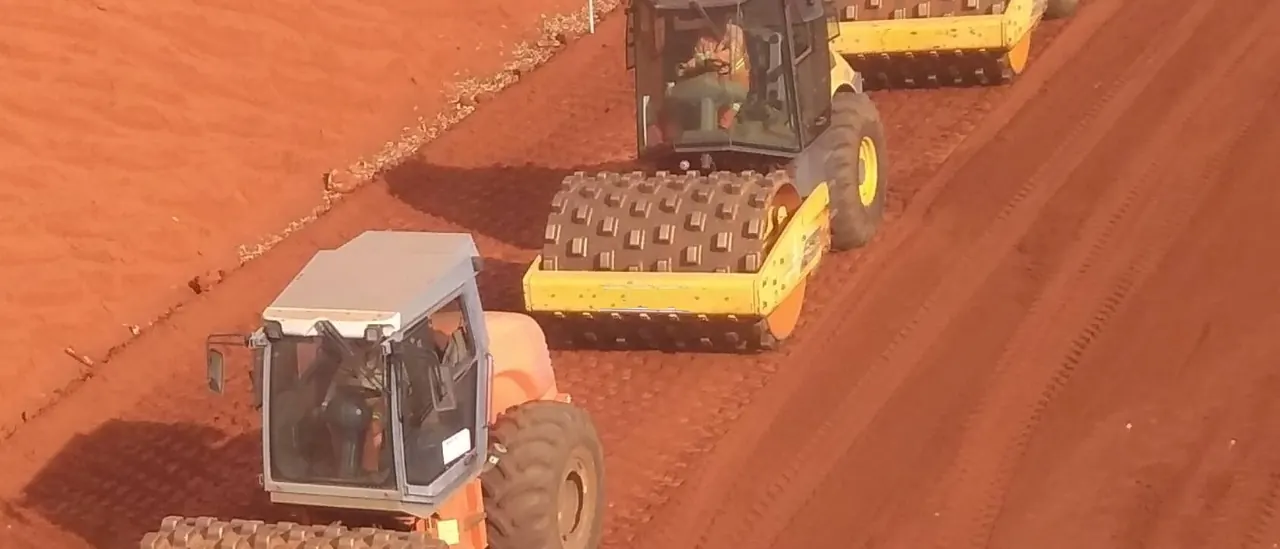 Três rolos compactadores pé de carneiro trabalhando em fila sobre plataforma de terra vermelha