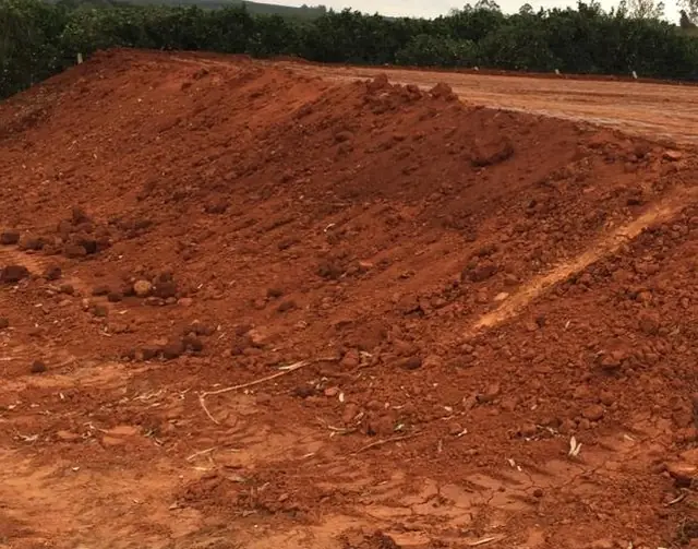 Plataforma de aterro de terra vermelha compactada ao lado de um pomar