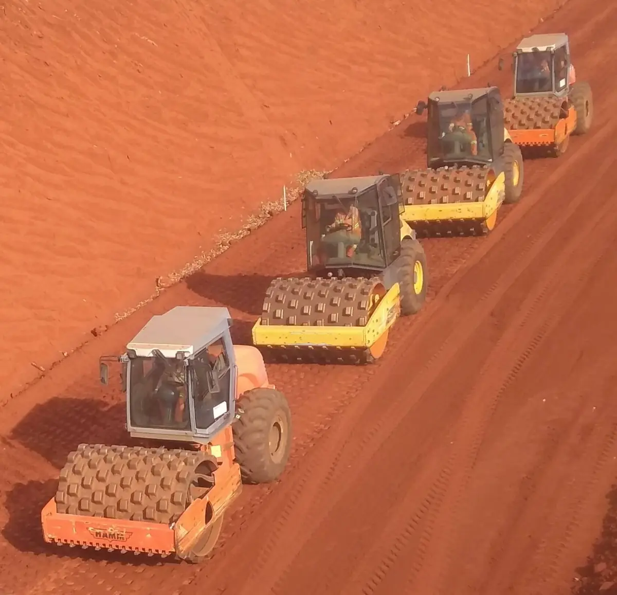 Três rolos compactadores pé de carneiro trabalhando em fila sobre plataforma de terra vermelha