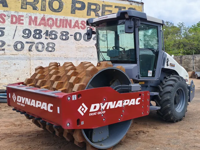 Rolo compactador pé de carneiro Dynapac CA 25 D com adesivo da Locadora Rio Preto, diante do muro pintado do pátio da empresa