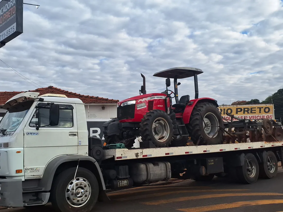 Trator Massey Ferguson vermelho sobre a prancha do caminhão da Locadora Rio Preto, com a grade acoplada