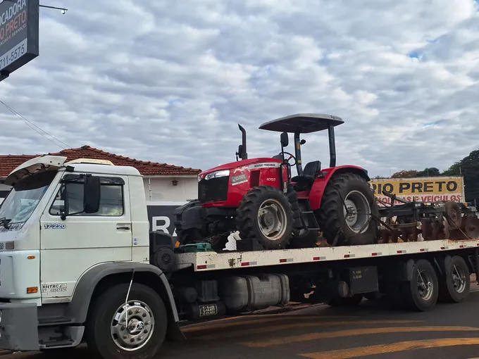 Trator Massey Ferguson vermelho sobre a prancha do caminhão da Locadora Rio Preto, com a grade acoplada